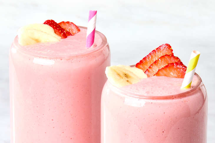 Head on shot of two glasses filled with strawberry banana smoothie in them, and garnished with sliced strawberries and bananas.